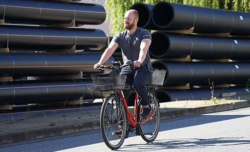 Gerodur Student Paul auf einem Fahrrad vor einem Stapel Rohre