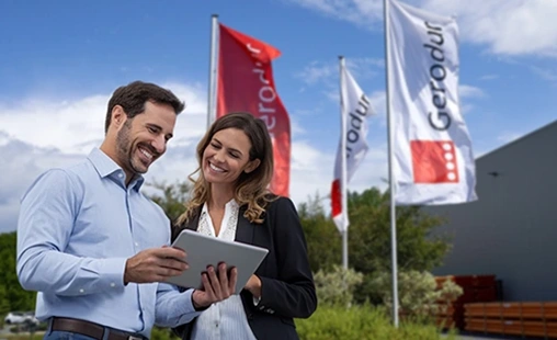 Zwei Mitarbeiter stehen mit einem Tablet vor den Gerodur Flaggen