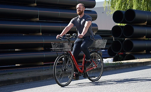 Gerodur Mitarbeiter fährt mit Fahrrad übers Gelände und an Rohren vorbei